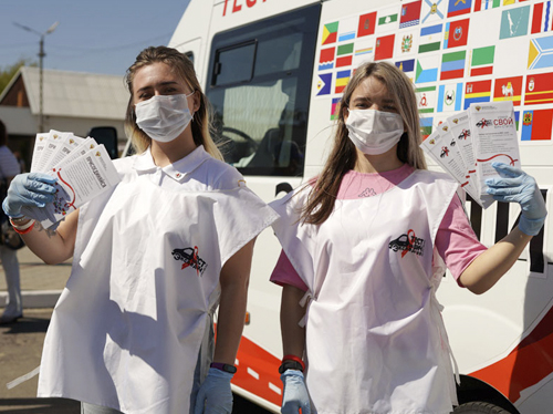 Две девушки в медицинских масках и белых накидках демонстрируют буклеты информационной кампании по профилактике ВИЧ/СПИДа 